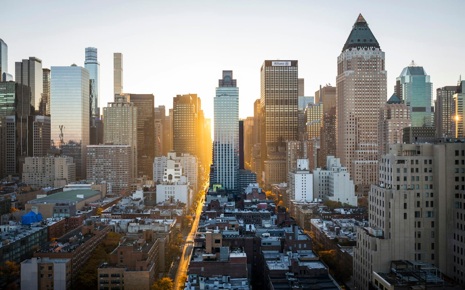 A dense city skyline in warm sunset light, with the sun flaring between towers