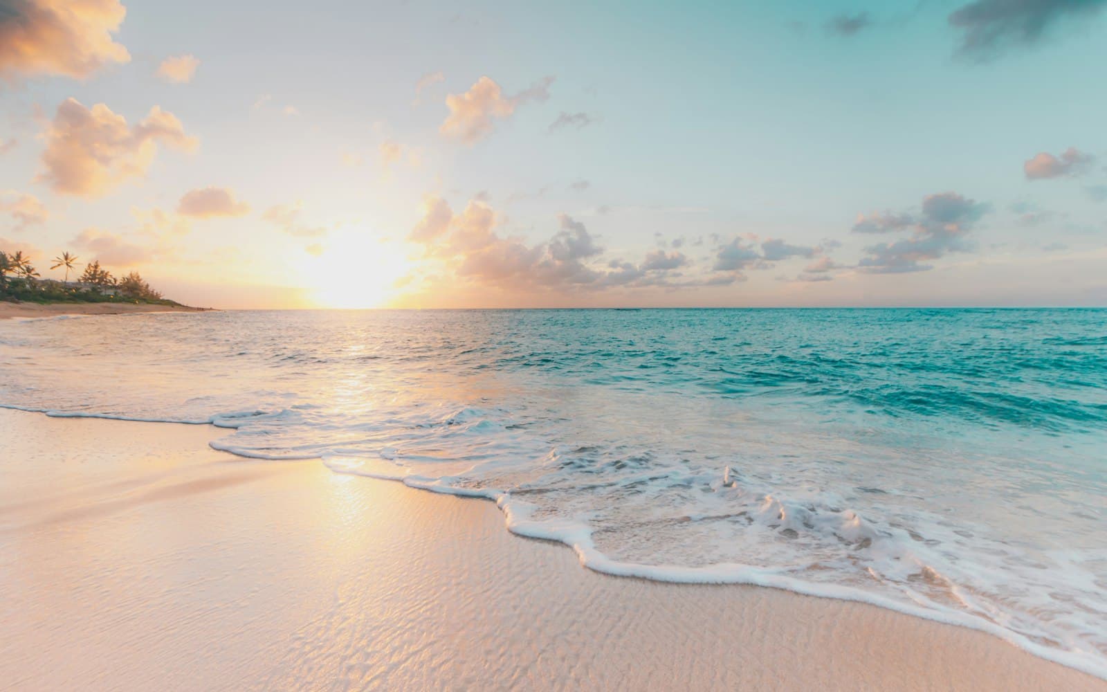 A quiet shoreline at sunrise, with a thin wave washing onto pale sand