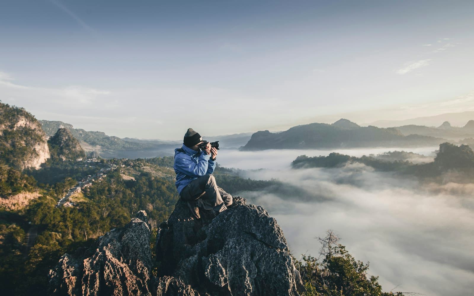 A person on a cliff photographing a mountain range above the clouds