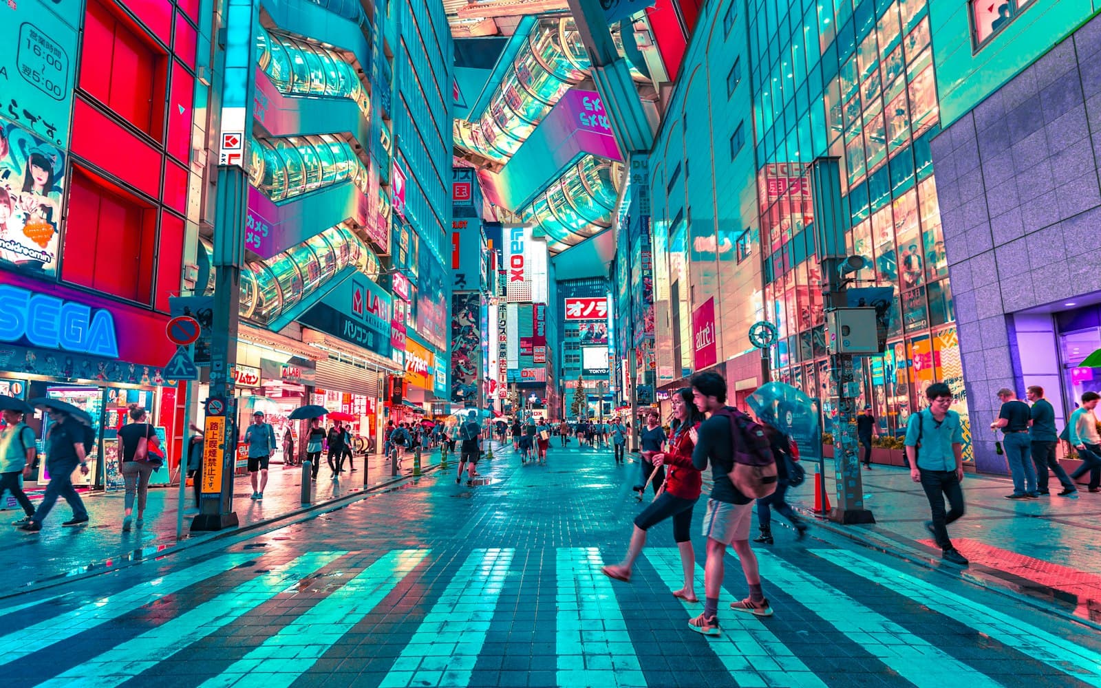 A neon shopping street at night, with crowds crossing wet pavement
