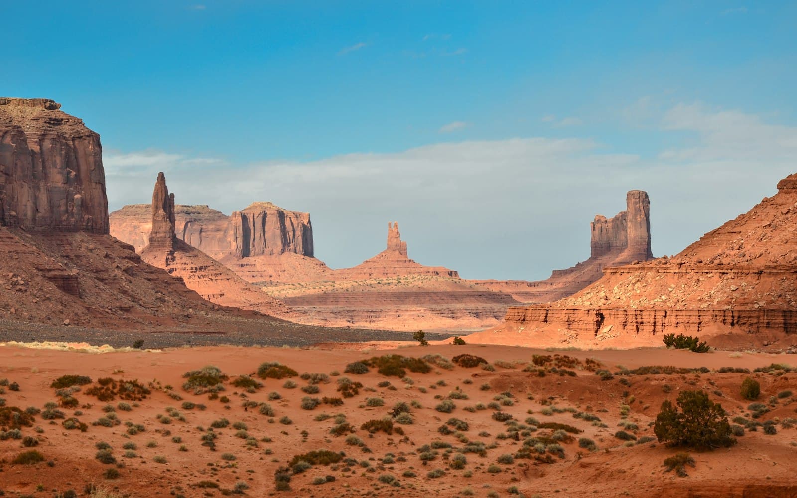 Red sandstone buttes rising from a desert valley under a pale blue sky